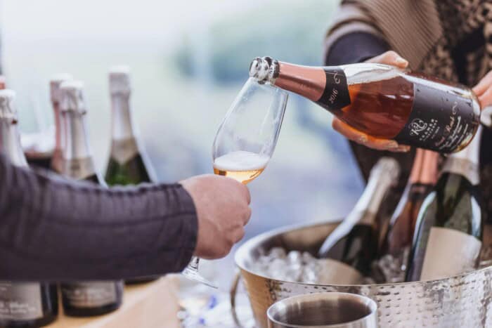 Hand pouring sparkling rosé wine from a Kramer Vineyards bottle into a flute over an ice bucket.